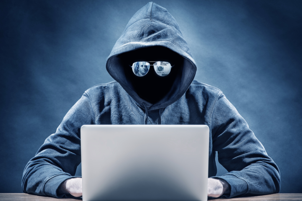 suspicious character in hoodie and sunglasses on laptop